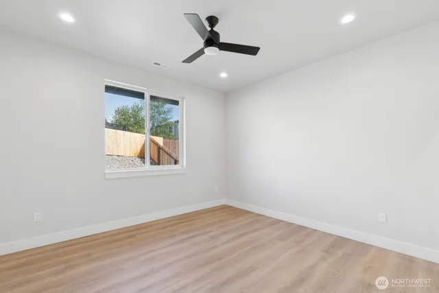 an empty room with wooden floor chandelier fan and windows