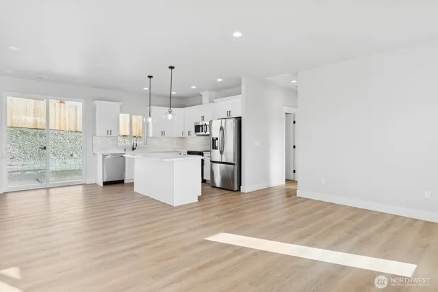 a view of a kitchen with stainless steel appliances granite countertop a stove top oven a refrigerator and white cabinets with wooden floor