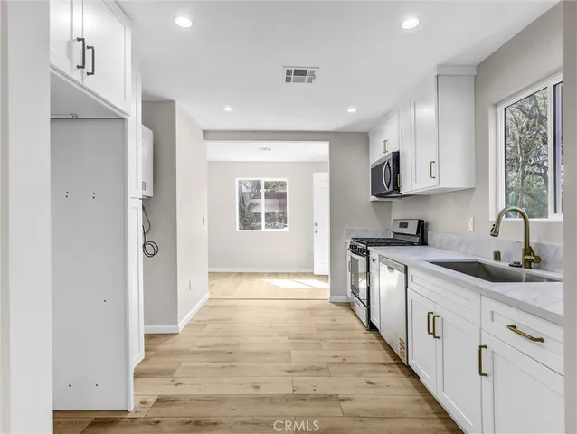 a large white kitchen with stainless steel appliances granite countertop a sink and dishwasher with wooden floor