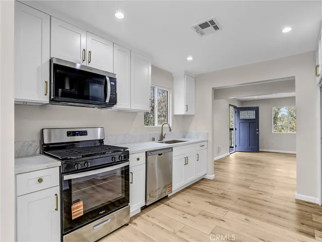a kitchen with stainless steel appliances granite countertop a stove top oven a sink dishwasher and white cabinets