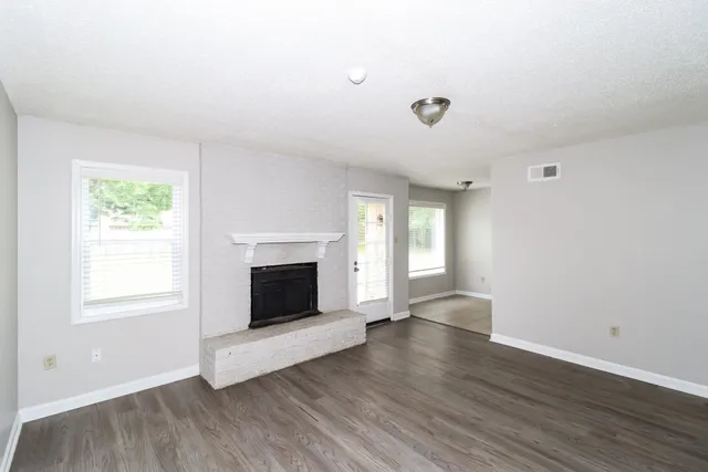 an empty room with wooden floor fireplace and windows