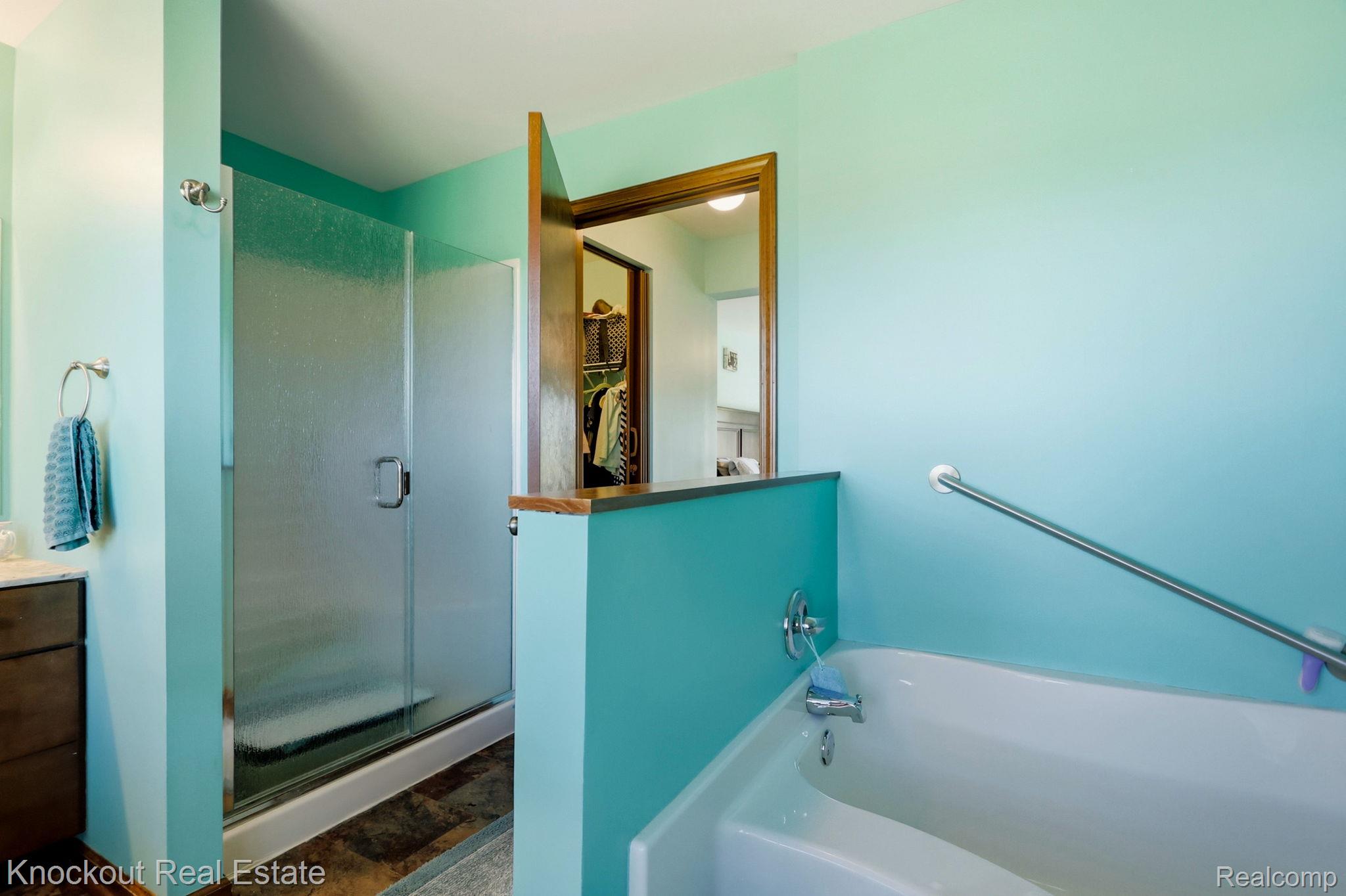 5727 Mackinaw Road Saginaw, MI 48604 - Photo 28 of 60 White soaking tub with grab bar, glass-enclosed shower, wood-finish flooring, and built-in vanity with under-sink storage