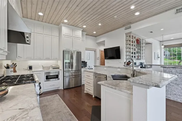 a kitchen with stainless steel appliances granite countertop a stove top oven a sink a refrigerator and white cabinets