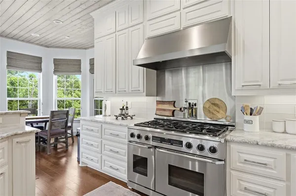 a kitchen with granite countertop a stove a sink dishwasher and white cabinets with wooden floor