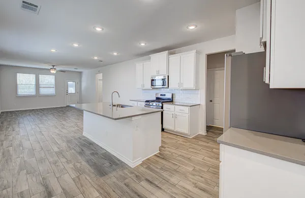 a kitchen with stainless steel appliances granite countertop a sink a stove a refrigerator and white cabinets with wooden floor