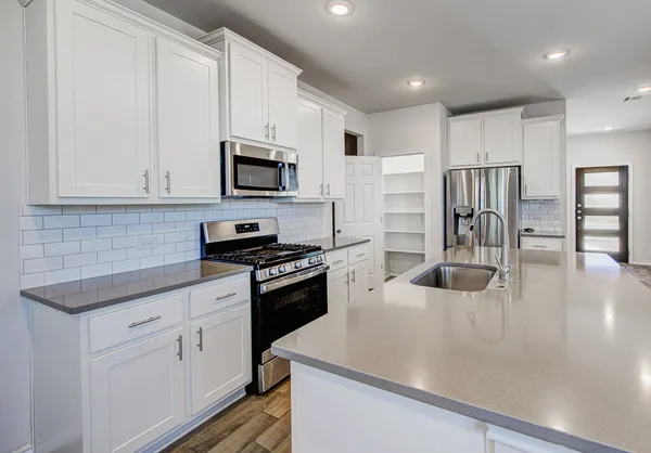 a kitchen with stainless steel appliances granite countertop a stove top oven a sink a refrigerator white cabinets and granite countertops with wooden floor