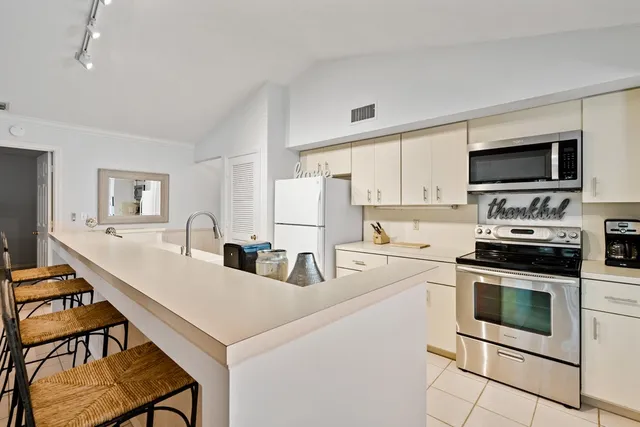 a kitchen with stainless steel appliances a stove top oven a sink a refrigerator white cabinets and chairs