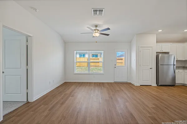 an empty room with wooden floor a ceiling fan and windows