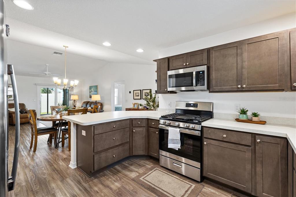 6767 Mary Loop The Villages, FL 34762 - Photo 7 of 26 a kitchen with stainless steel appliances granite countertop a stove top oven a sink dishwasher a refrigerator and a dining table with wooden floor
