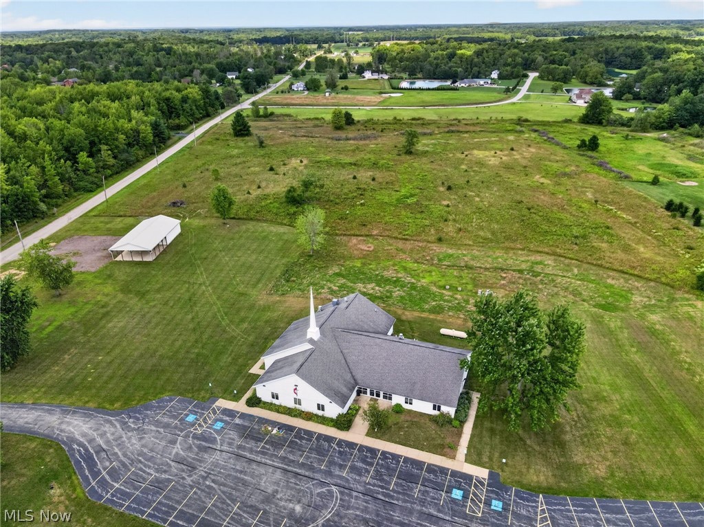 Expansive property featuring a paved parking area, a white structure with a dark roof, a separate large covered structure, and surrounding open green space