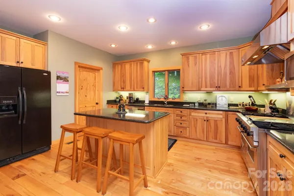 a kitchen with stainless steel appliances granite countertop wooden cabinets a sink a stove a refrigerator and island with wooden floor
