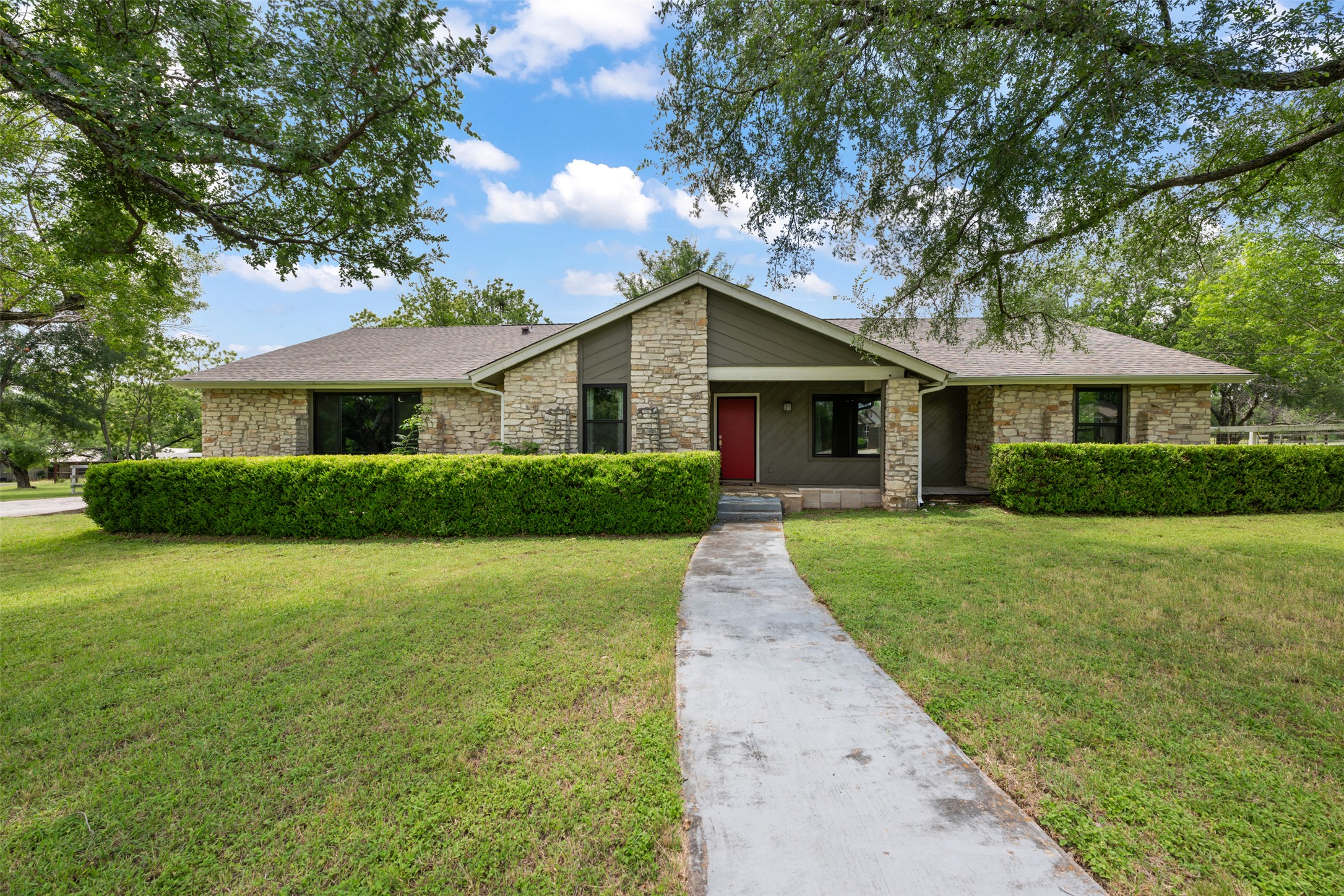 1600 Pin Oak Lane Round Rock, TX 78681 - Photo 1 of 40 Exterior featuring stone facade, a red entry door, dark-framed windows, mature trees, and a concrete pathway