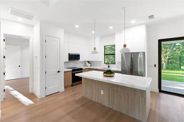 a kitchen with stainless steel appliances kitchen island granite countertop a sink a stove and a wooden floors