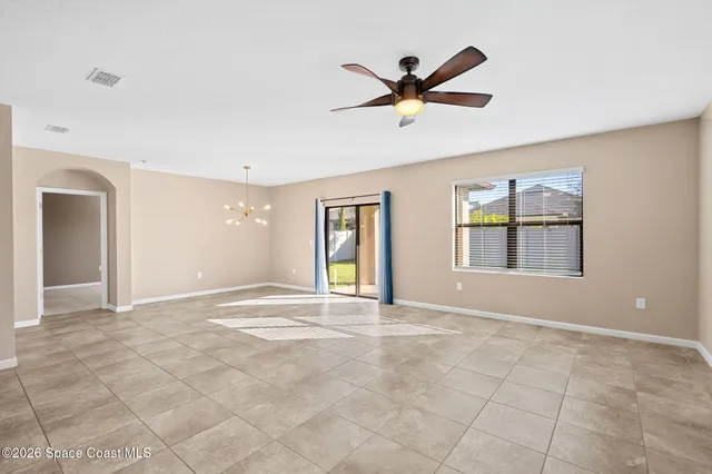 a view of an empty room with window and chandelier fan