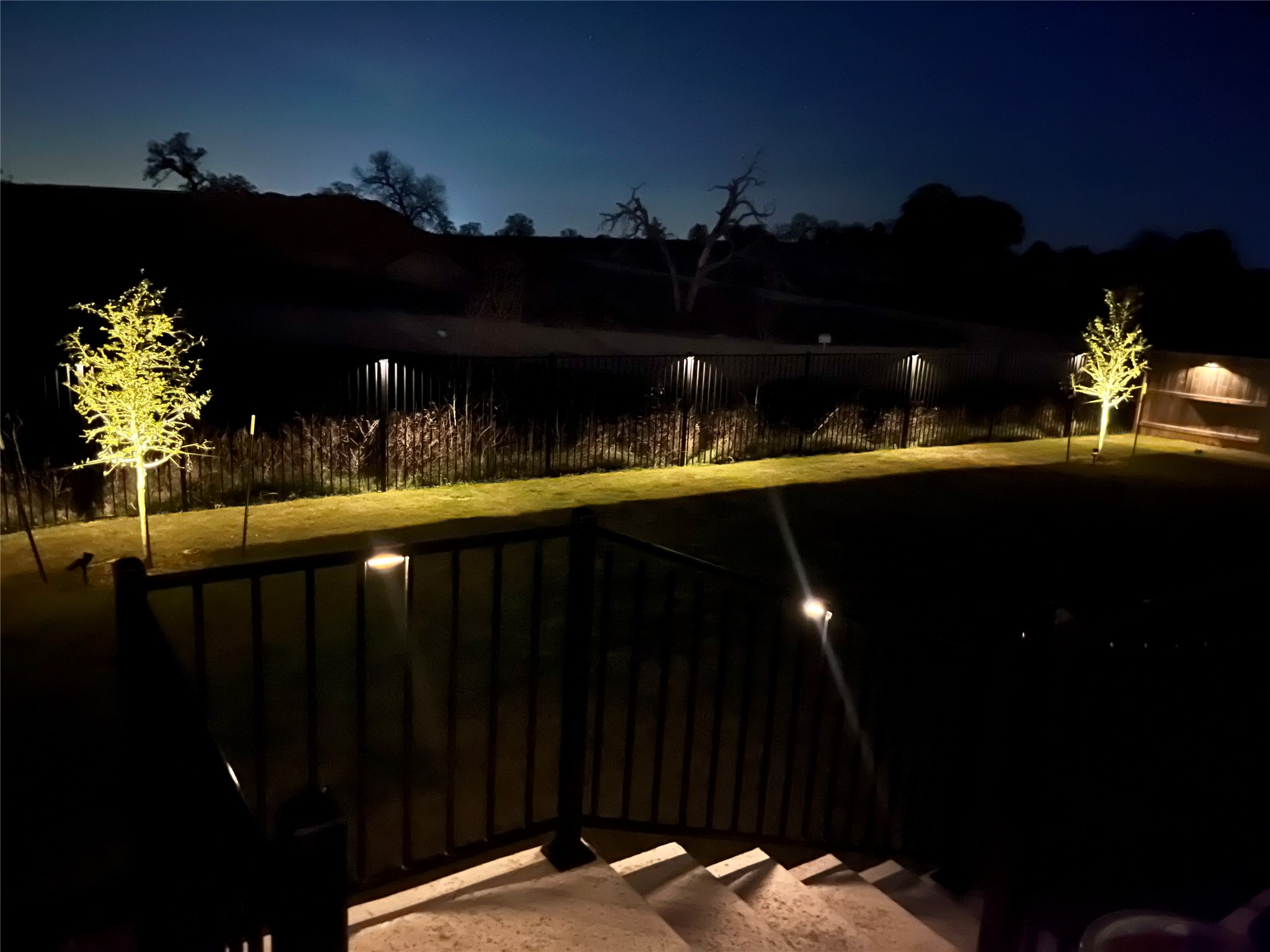 130 Firethorn Loop Bastrop, TX 78602 - Photo 36 of 38 Illuminated backyard landscaping creates an inviting ambiance under the twilight sky.