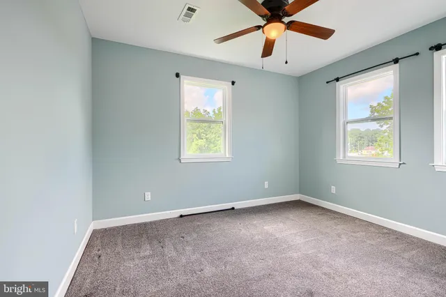an empty room with chandelier fan and windows