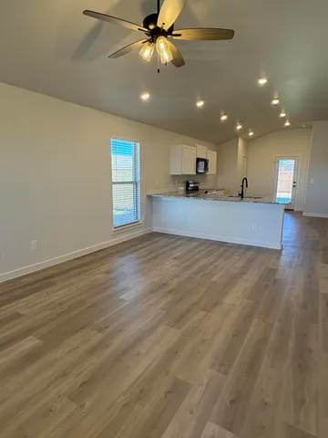 an empty room with wooden floor a ceiling fan and kitchen view