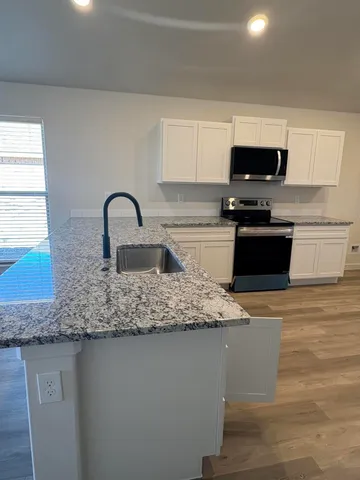 a kitchen with kitchen island granite countertop a sink a stove top oven a counter space and cabinets