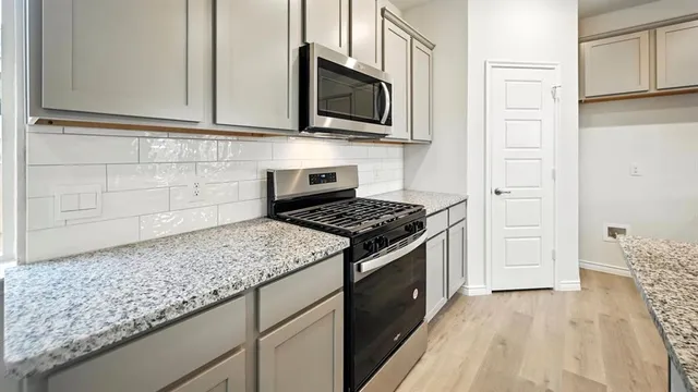 an empty room with wooden floor and kitchen view