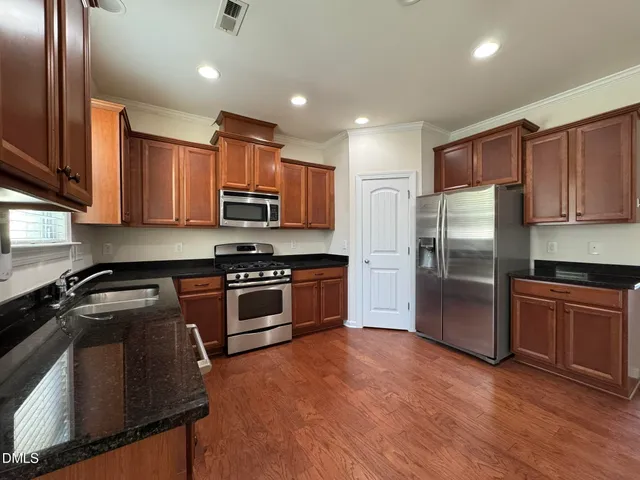 a kitchen with stainless steel appliances granite countertop a refrigerator a stove and a sink with wooden floor