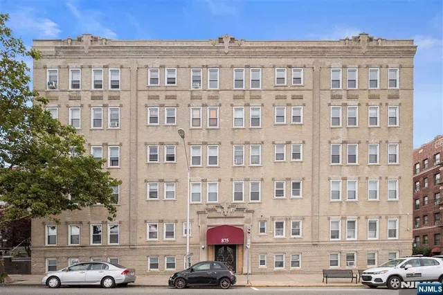 a front view of a building with lot of cars and trees