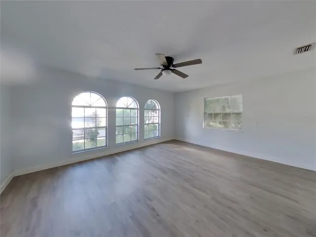 an empty room with wooden floor fan and windows