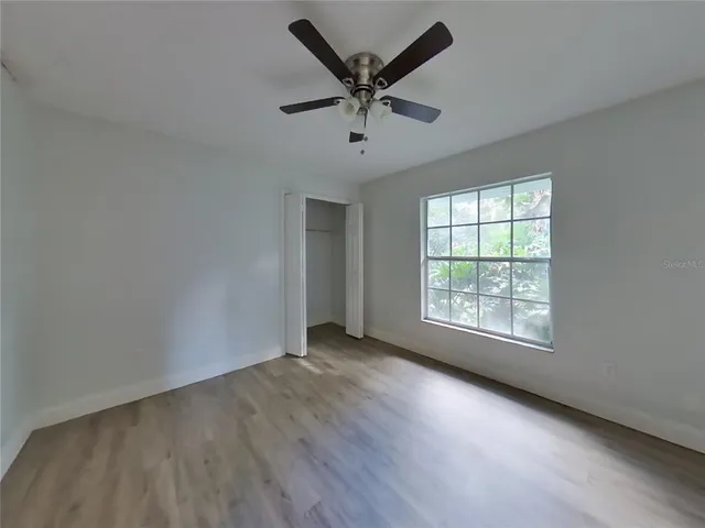 an empty room with wooden floor fan and windows