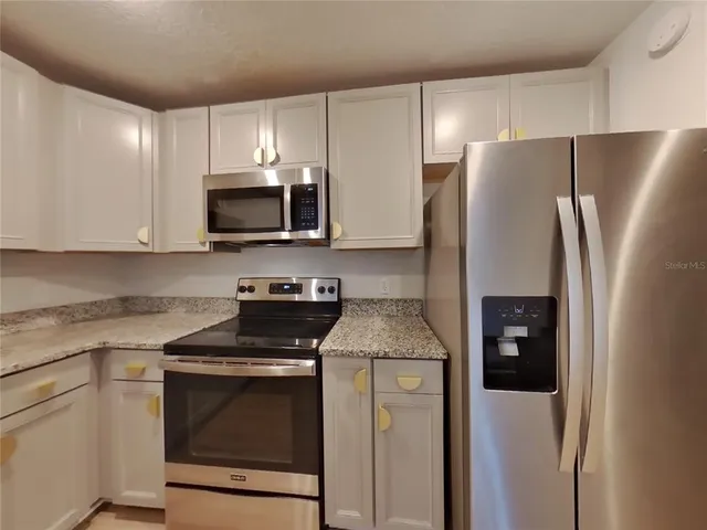 a kitchen with stainless steel appliances granite countertop white cabinets a refrigerator and a stove top oven