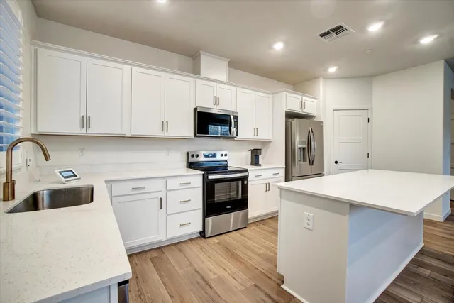 a kitchen with stainless steel appliances white cabinets a sink a stove a refrigerator and island with wooden floor