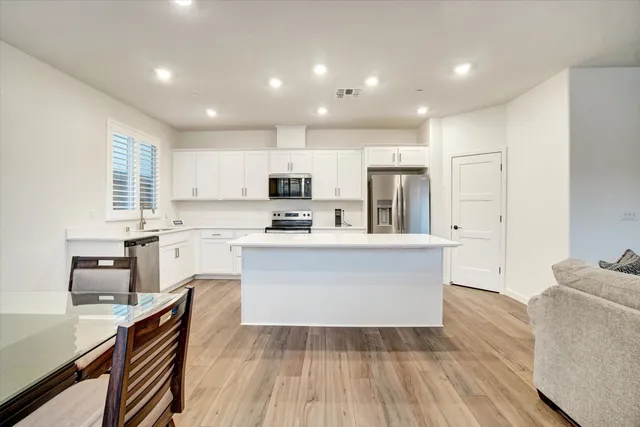 a large kitchen with kitchen island granite countertop a stove a sink a refrigerator and white cabinets with wooden floor