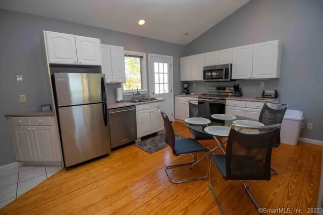 a kitchen with stainless steel appliances granite countertop a refrigerator a stove a sink dishwasher and white cabinets with wooden floor