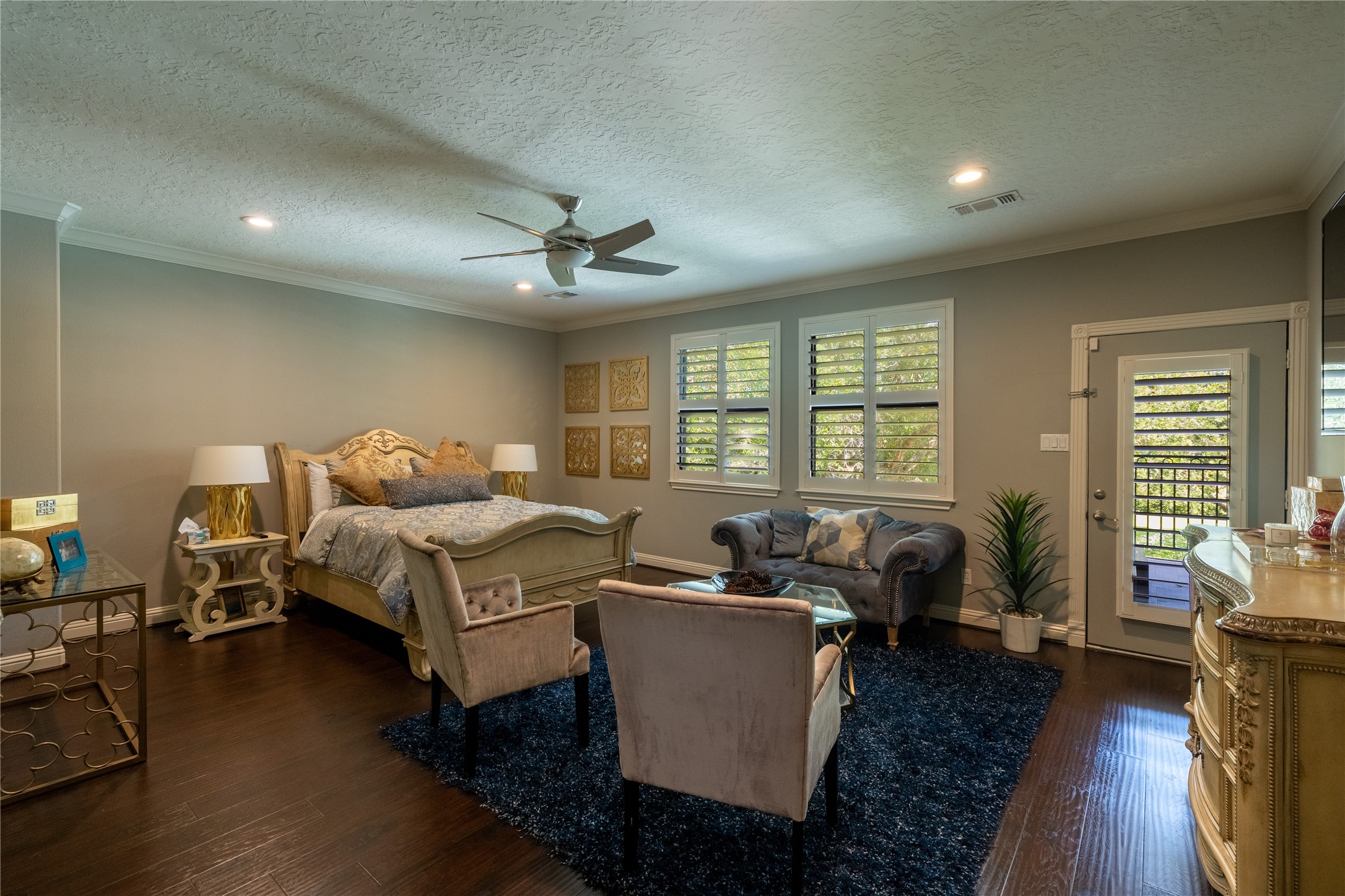 4002 Silver Ridge Boulevard Missouri City, TX 77459 - Photo 23 of 50 This is a spacious bedroom featuring hardwood floors, comfortable seating areas, and ample natural light from windows with plantation shutters. There's also direct access to the outdoors through a glass-paneled door. The room is finished with a ceiling fan and recessed lighting.