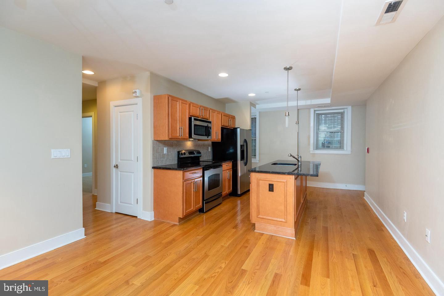 4300 Spruce Street, Unit A102 Philadelphia, PA 19104 - Photo 3 of 16 a large kitchen with stainless steel appliances kitchen island granite countertop a refrigerator a stove top oven a sink dishwasher and white cabinets with wooden floor