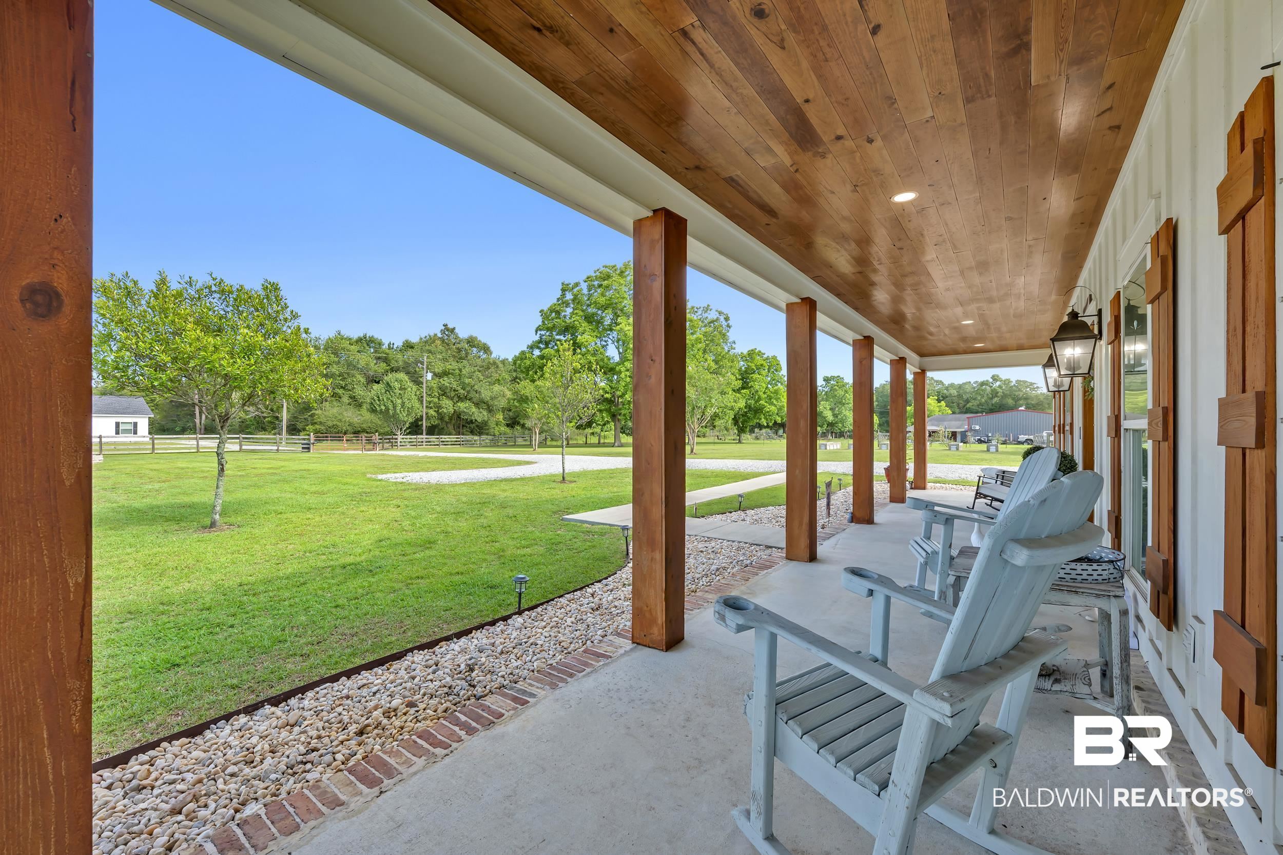 6576 Ranch Loop Road East Grand Bay, AL 36541 - Photo 8 of 39 Expansive covered porch featuring a wood-planked ceiling, substantial wood support columns, concrete flooring, and exterior wall lanterns