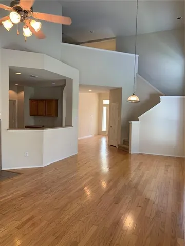 a view of an empty room with wooden floor and a kitchen