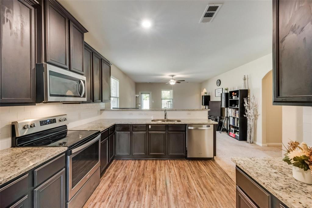 2213 Georgetown Street Princeton, TX 75407 - Photo 5 of 25 Kitchen with stainless steel appliances, dark brown cabinetry, a peninsula, and light stone counters