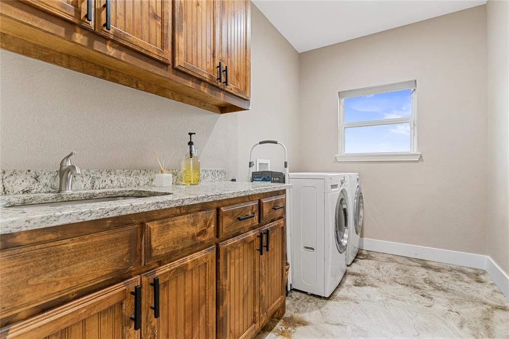 139 Kriston Lane Springtown, TX 76082 - Photo 13 of 39 Laundry area featuring wood-finish cabinetry, a stone-finish countertop with an undermount sink, a chrome faucet, and a window