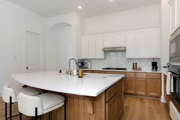 a kitchen with a stove a sink a refrigerator and white cabinets with wooden floor