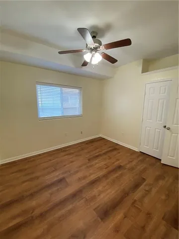 a view of an empty room with wooden floor and a ceiling fan