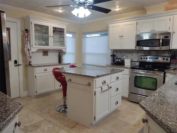 a kitchen with stainless steel appliances kitchen island granite countertop a sink dishwasher stove and white cabinets with wooden floor