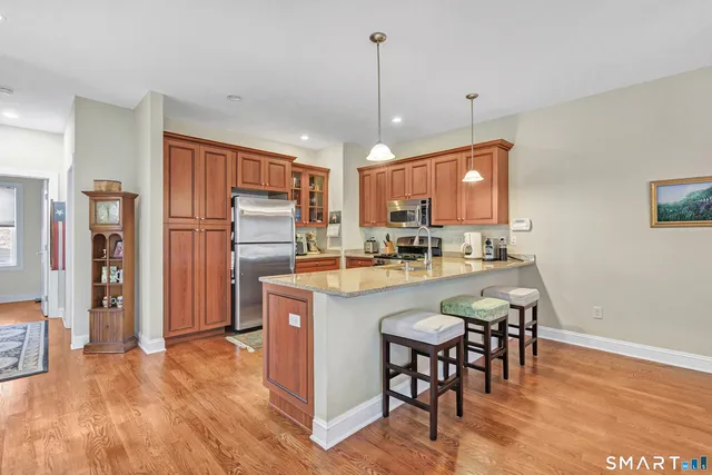 a kitchen with stainless steel appliances granite countertop a refrigerator a oven a sink a dining table and chairs with wooden floor