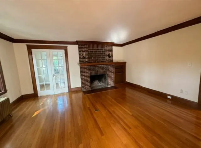 a view of an empty room with wooden floor fireplace and a window