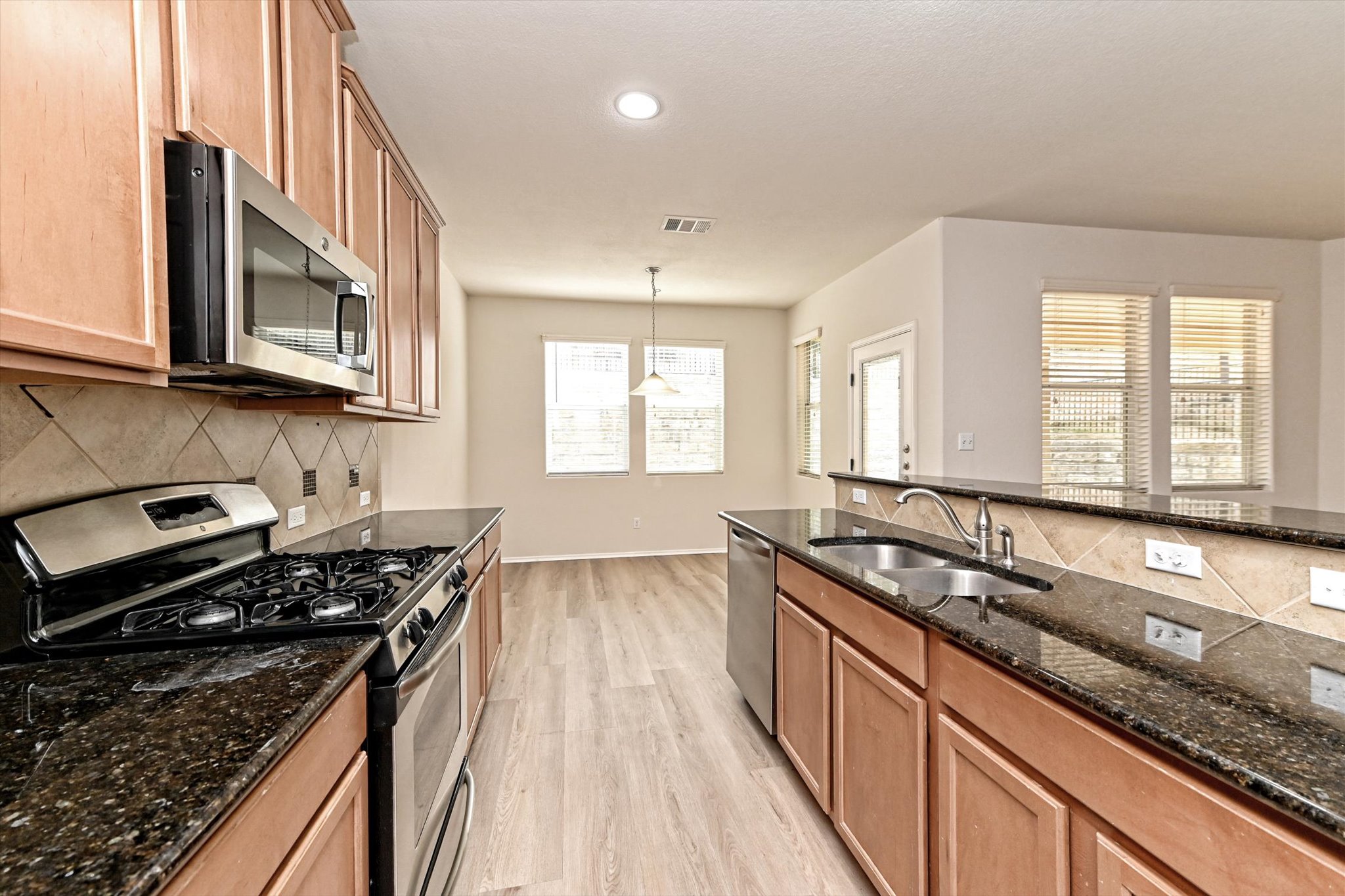 31 Stone Terrace Drive Austin, TX 78734 - Photo 11 of 29 Kitchen featuring stainless steel appliances, dark stone counters, light wood-style floors, wood finish cabinets, and decorative backsplash