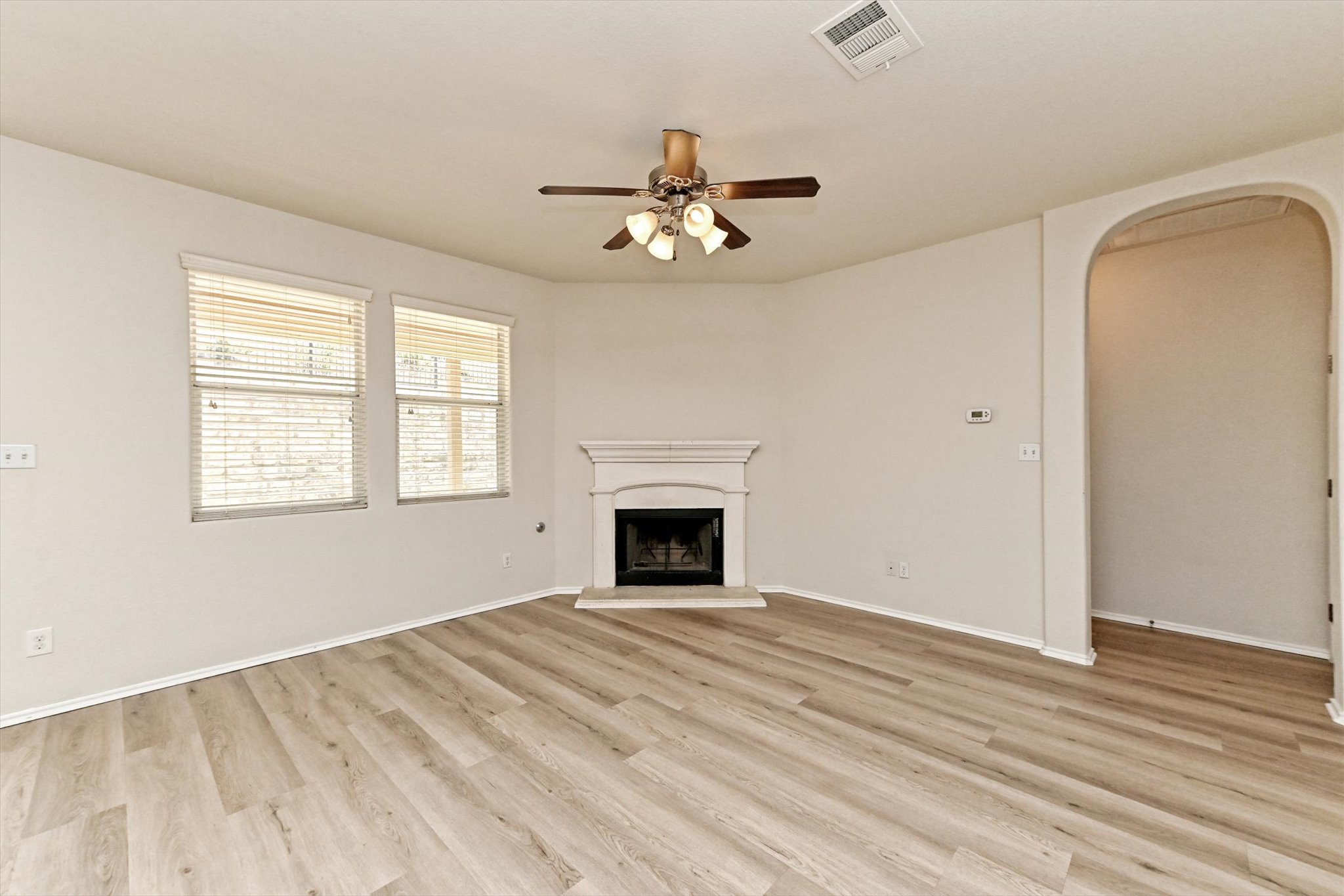 31 Stone Terrace Drive Austin, TX 78734 - Photo 6 of 29 Unfurnished living room featuring arched walkways, ceiling fan, a fireplace with raised hearth, and light wood-type flooring