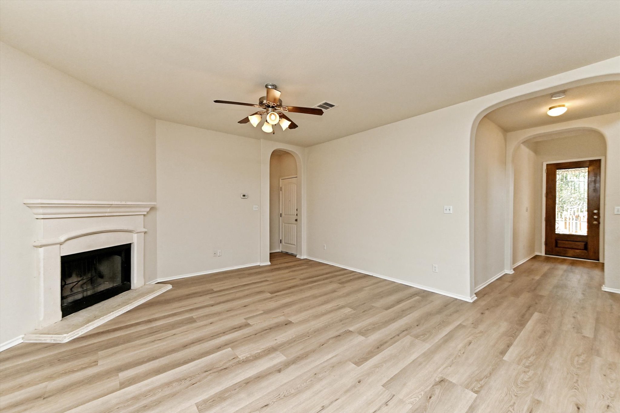 31 Stone Terrace Drive Austin, TX 78734 - Photo 7 of 29 Unfurnished living room with arched walkways, a fireplace with raised hearth, light wood-style floors, and a ceiling fan