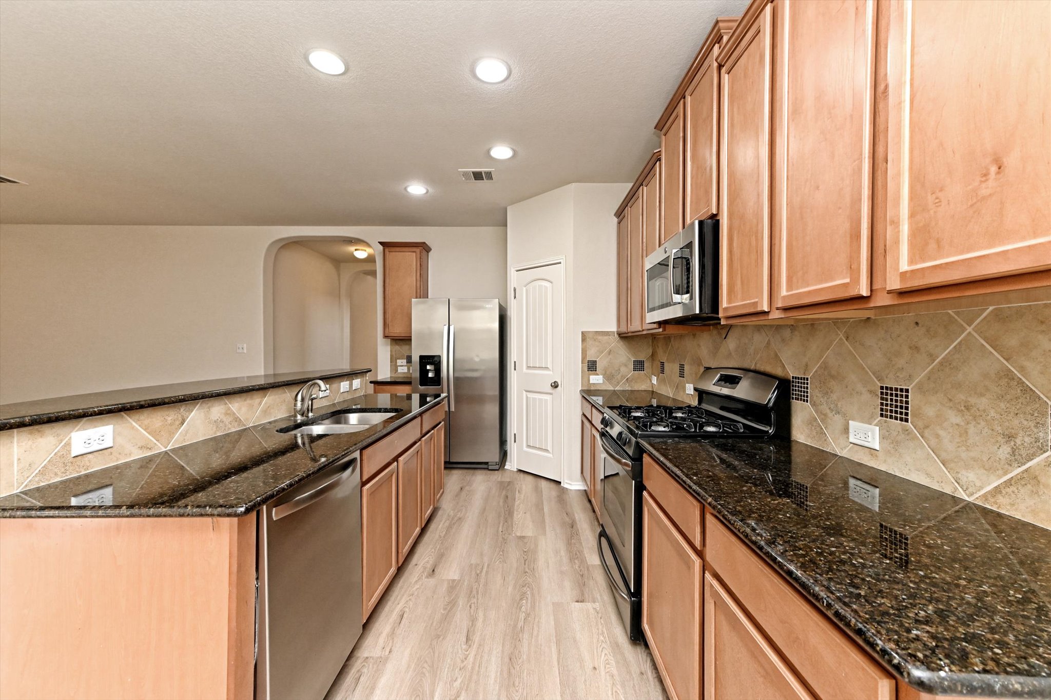 31 Stone Terrace Drive Austin, TX 78734 - Photo 9 of 29 Kitchen featuring stainless steel appliances, light wood-style floors, a kitchen island with sink, dark stone countertops, and arched walkways