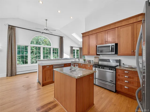 a kitchen with stainless steel appliances granite countertop wooden cabinets a refrigerator a stove a sink and dishwasher with wooden floor