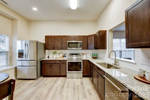 a large kitchen with stainless steel appliances granite countertop a stove top oven a sink dishwasher and a refrigerator with wooden floor