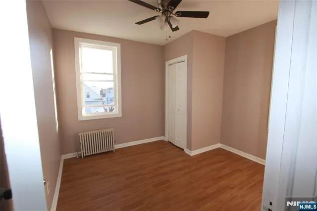 an empty room with wooden floor windows and fan