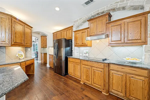 a kitchen with stainless steel appliances granite countertop a refrigerator a sink dishwasher and wooden cabinets with wooden floor